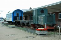 První motorová lokomotiva z Wangerooge spolu s plošinovým nákladním a starším osobním vozem před odbavovací halou přístavu Harlesiel.